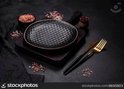 Black empty plate, cutlery and napkin on a stone table top view. Table setting. Empty black plate over dark stone background with free space
