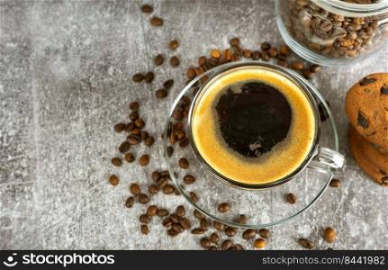 Black espresso coffee in a glass with cream on gray background with scattering of coffee beans. Top view, flat lay with copy space.. Espresso coffee in a glass with coffee cream.