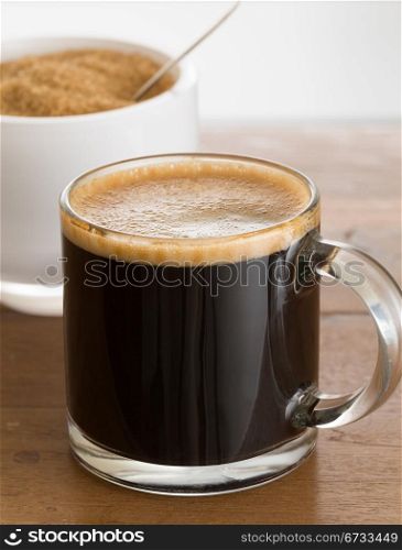 Black expresso coffee in small glass cup with sugar in white bowl reflecting