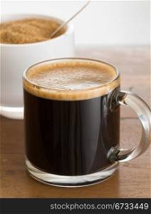 Black expresso coffee in small glass cup with sugar in white bowl reflecting