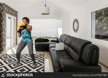 Black female athlete in sportswear and boxing gloves doing exercises during workout at home with dogs. Determined woman training in boxing gloves at home