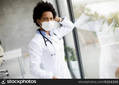 Black female doctor standing by the medical office window with facial protective mask