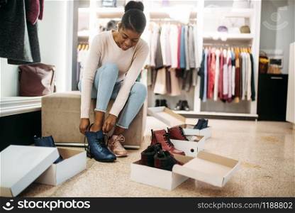Black female person trying on shoes, shopping. Shopaholic in clothing store, consumerism lifestyle, fashion