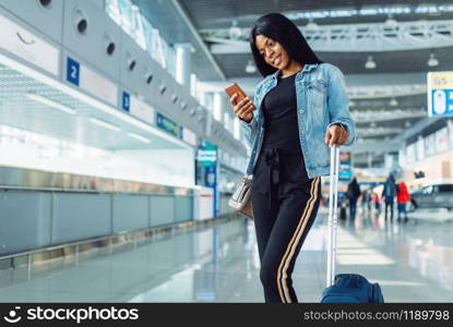 Black female tourist with suitcase and phone waiting for departure in international airport. Passenger with baggage in air terminal, happy journey sexy lady, summer travel of happy woman