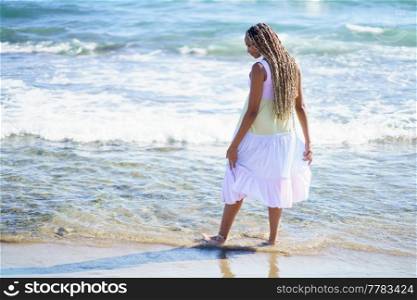 Black female walking along the shore of the beach wearing a beautiful long dress. Young girl enjoying her vacations.. Black female walking along the shore of the beach wearing a beautiful long dress.