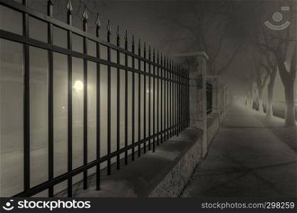 black fence along foggy city pavement