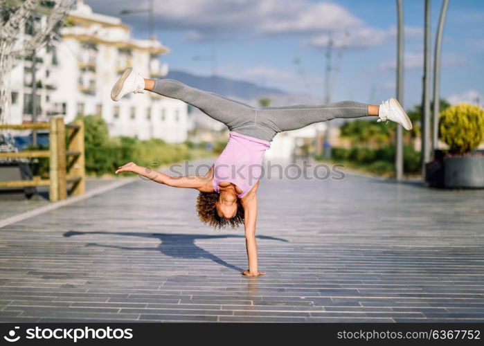 Black fit woman doing fitness acrobatics in urban background. Young female exercising and working out hard.