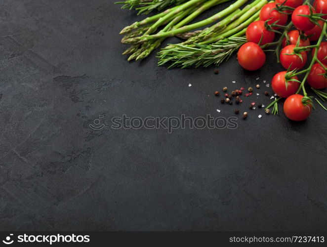Black food background with asparagus, cherry tomatoes and rosemary on black table background with black pepper. Space for text
