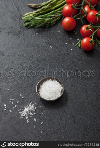 Black food background with asparagus, cherry tomatoes and rosemary on black table background with bowl of salt. Vertical