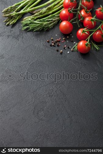 Black food background with asparagus, cherry tomatoes and rosemary on black table background with black pepper.