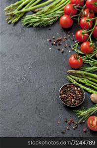 Black food background with healthy organic asparagus, cherry tomatoes and rosemary on black table background with bowl of pepper. Vertical