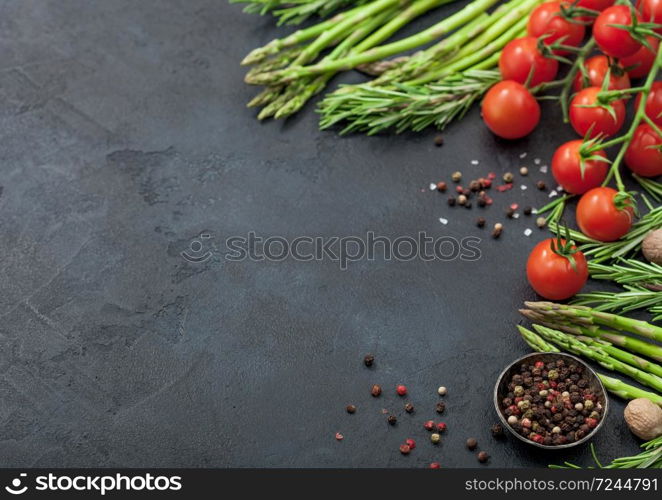 Black food background with healthy organic asparagus, cherry tomatoes and rosemary on black table background with bowl of pepper. Space for text