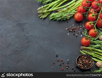 Black food background with healthy organic asparagus, cherry tomatoes and rosemary on black table background with bowl of pepper. Space for text