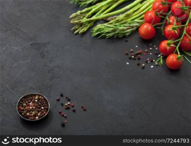 Black food background with healthy organic asparagus, cherry tomatoes and rosemary on black table background with bowl of pepper.