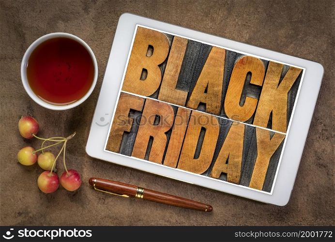 Black Friday - holiday shopping concept - word abstract in vintage letterpress wood type on a digital tablet with a cup of tea and crab apples