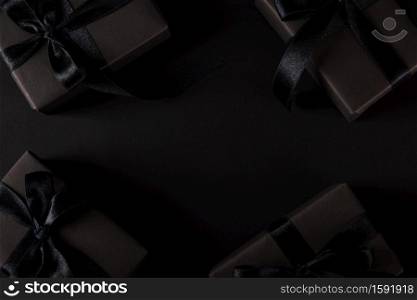 Black Friday sale shopping concept, Top view of gift box wrapped black paper and black bow ribbon present around free copy space for text, studio shot on dark background