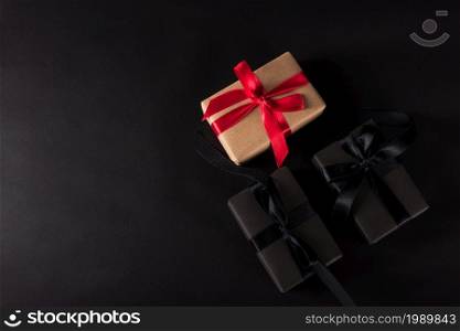 Black Friday Sale shopping concept, Top view of gift box wrapped black paper and black bow ribbon present around the brown box with red bow ribbon, studio shot on dark background