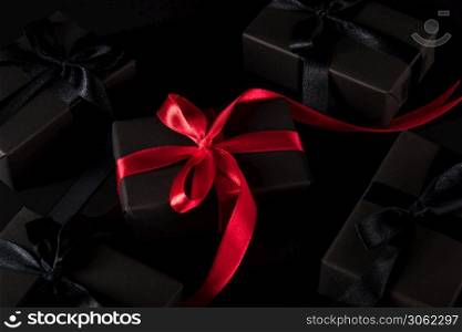 Black Friday sale shopping concept, Top view of gift box wrapped black paper and black bow ribbon present around the box with a red ribbon, studio shot on dark background