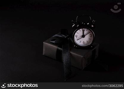 Black Friday sale shopping concept, Top view of gift box wrapped in black paper and black bow ribbon and black alarm clock, studio shot on black background