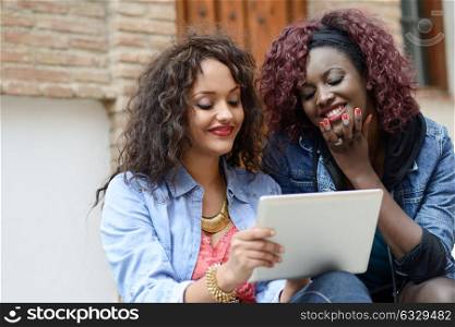 Black girls with tablet computer in urban backgrund. Friends talking wearing casual clothes