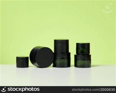 black glass jars for cosmetics on a white table. Packaging for cream, gel, serum, advertising and product promotion, mock up