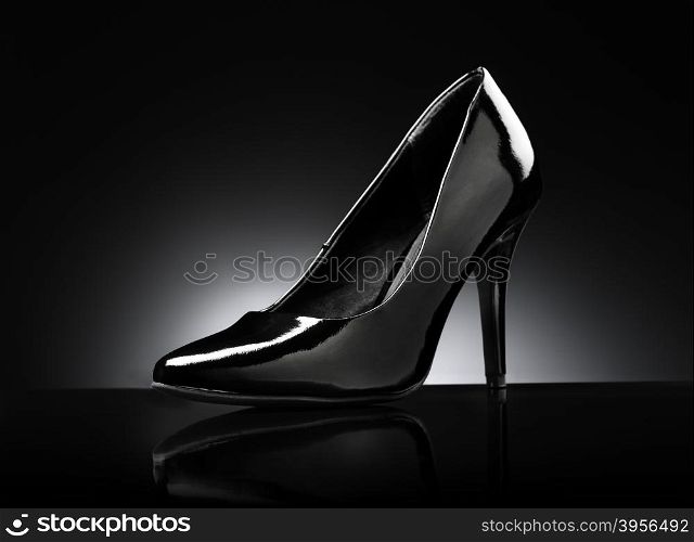 Black glossy ladies stiletto heel pump on black reflective background.