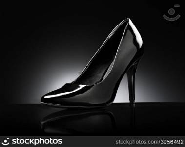 Black glossy ladies stiletto heel pump on black reflective background.