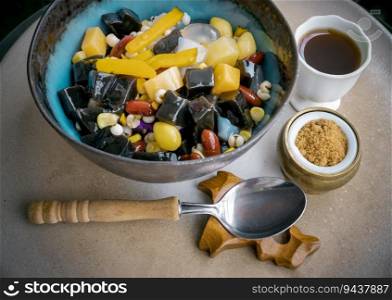 Black Grass Jelly is including Nuts, Cereals, Red beans, Ginkgo, Sliced   pumpkin, Corn kernels, Millet, Diced sweet potato, Palm seed and Jelly which is served with Longan Juice and Brown sugar on ceramic tray. Traditional iced sweet dessert, Selective focus.