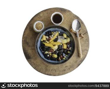 Black Grass Jelly is including Nuts, Cereals, Red beans, Ginkgo, Sliced   pumpkin, Corn kernels, Millet, Sweet potato, Palm seed and Jelly served with Longan juice, Brown sugar and spoon on Old round wood cutting board isolated on white background with clipping path. Traditional iced sweet dessert, Top view, Selective focus.
