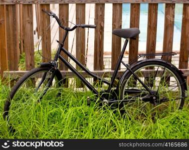 black grunge bicycle aged on a wood fence and grass