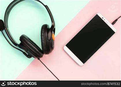 Black headphones and smartphone lies on a colorful pastel pink background. Music listening concept. Portable technology. Flat lay top view. Black headphones and smartphone lies on a colorful pastel pink background