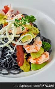 Black Italian seafood pasta with shrimps, cherry tomatoes and greens. Pasta with cuttlefish ink, cooked sea food macaroni.