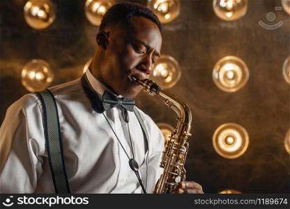 Black jazz performer plays the saxophone on the stage with spotlights. Black jazzman preforming on the scene. Black jazz performer plays the saxophone on stage