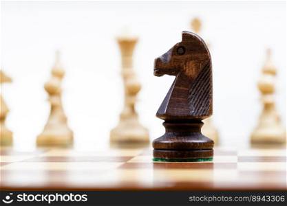 black knight against white chess figures in background on wooden chessboard close up  focus on queen 