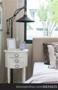 black lamp, picture frame and alarm clock on bedside table