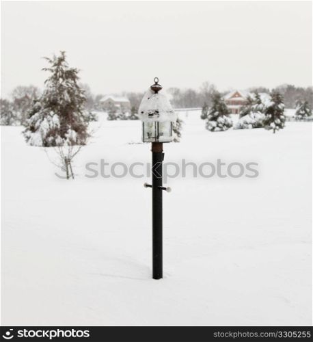 Black lamp post buried in deep snow by covered road