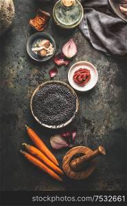 Black lentils with cooking ingredients for tasty vegan dishes on dark background. Top view. Healthy vegetarian eating concept. Horizontal banner. Plant based protein source. Top view