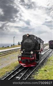 Black locomotive with red color driving on a railtrack under a cloudy sky