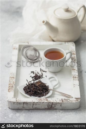 Black loose tea with tea ball strainer infuser and ceramic teapot with cup in white wooden box