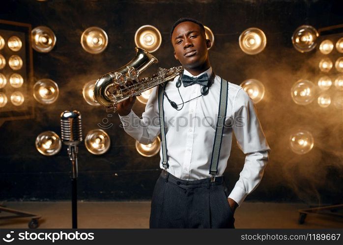 Black male jazz performer poses with saxophone on the stage with spotlights. Black jazzman preforming on the scene. Black jazz performer poses with saxophone on stage