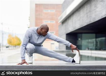 Black man doing stretching before running in urban background. Young male exercising