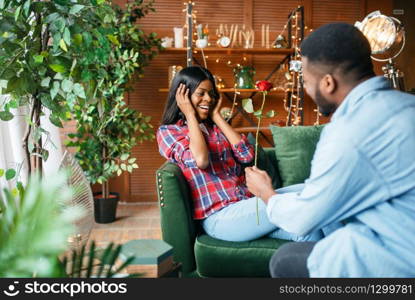 Black man gives red rose to his woman, romantic meeting at home. Happy african love couple leisures in their house