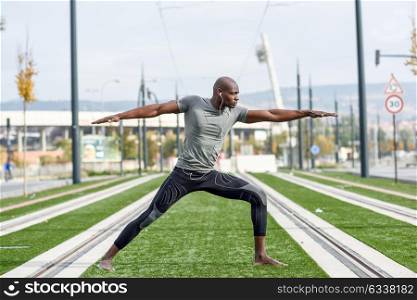 Black man practicing yoga in urban background. African male doing workout outdoors.