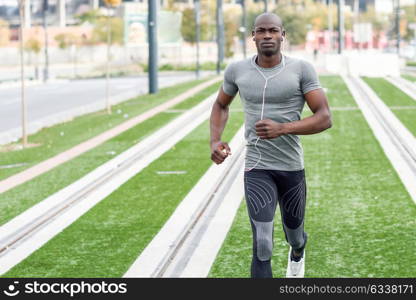 Black man running and listening to music in urban background. Handsome male doing workout outdoors.