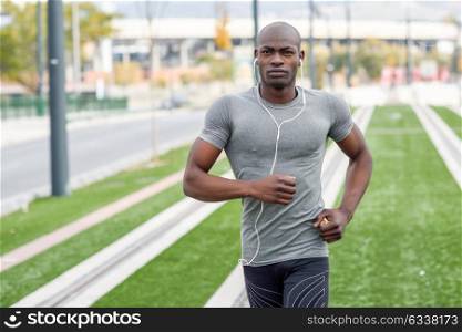 Black man running and listening to music in urban background. Handsome male doing workout outdoors.