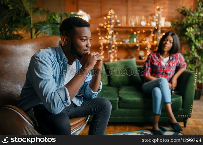 Black man sitting in a comfortable leather chair against his woman on the couch in the living room, relaxation at home. Young african american love couple leisures in their house