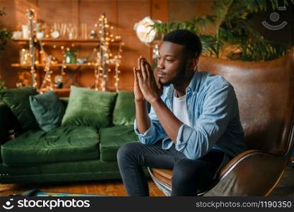 Black man sitting in a comfortable leather chair in the living room, relaxation at home. Young african american male person in his house. Black man sitting in a comfortable leather chair