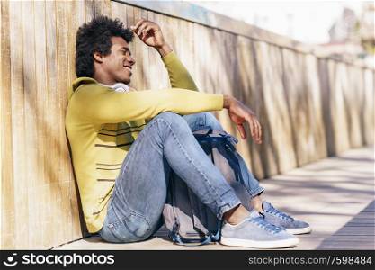 Black man with afro hair and headphones resting sitting on the ground.. Black man with afro hair and headphones resting on the ground.
