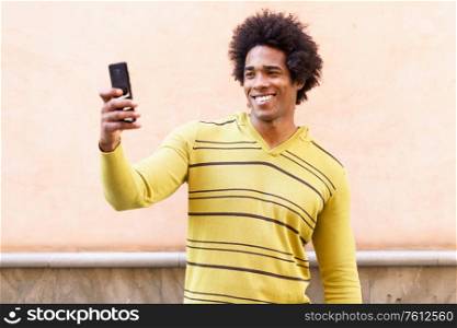 Black man with afro hair and headphones using smartphone taking photographs. Black man with afro hair and headphones using smartphone.