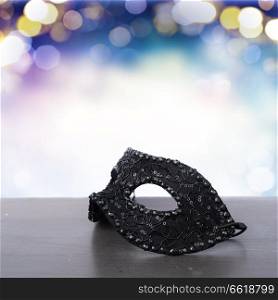 Black mask on wooden table border on blue bokeh background with copy space. Mask with masquerade decorations